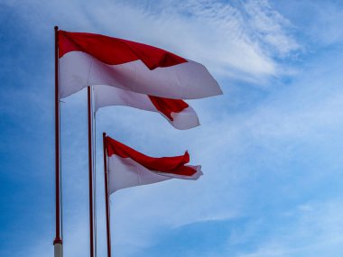 Endonezya bayrağı rüzgâr tarafından dalgalanan bir direkte mavi gökyüzü ve bulutlardan oluşan bir arka planda dalgalanıyor. Ulusal gurur ve bağımsızlığı sembolize ediyor. alçak açı ve arka planda yumuşak gün ışığı.