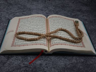 Balikpapan-Endonezya 5 Ağustos 2025 Kutsal Kur 'an, Arapça el yazısı ve ahşap masa üzerinde tespih anlamına gelir..