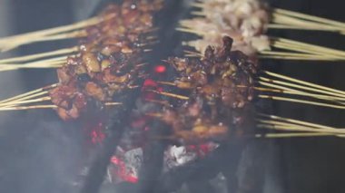 Satay satıcısı satay tezgahıyla ilgileniyor ve satayın iyice kızardığından emin oluyor. Satay, bambu çubuğuyla şişlenmiş baharatlı et veya tavuktur..