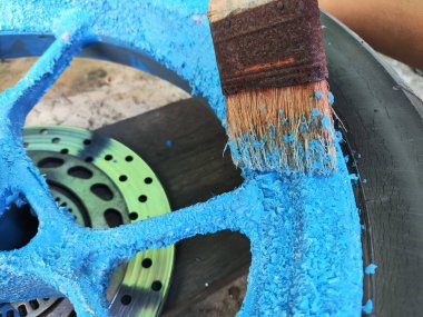 Motosiklet tekerleğinin kenarına boya çıkarıcı sürerken paslı bir fırçanın yakın plan çekimi. Bu fotoğraf DIY 'in, araç özelleştirmesinin ve yaratıcı projelerin harika bir temsili..