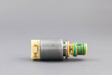 Katı gri arka planda sarı plastik konnektörü olan bir Allison Solenoid vanası. Fotoğraf, bu endüstriyel bölümün teknik detaylarını ve yıpranmış durumunu vurgulayan yakın plan bir fotoğraf..