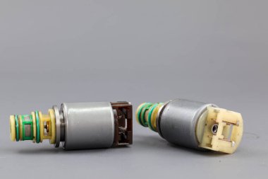 İki Allison iletim solenoid vanası gri bir arka planda gösteriliyor, biri dik duruyor ve diğeri yan tarafında. Fotoğraf metal gövdelerini, kablolarını ve konnektörlerini vurguluyor..