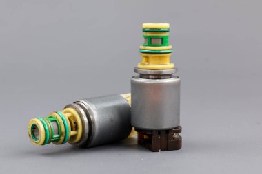 İki Allison iletim solenoid vanası gri bir arka planda gösteriliyor, biri dik duruyor ve diğeri yan tarafında. Fotoğraf metal gövdelerini, kablolarını ve konnektörlerini vurguluyor..