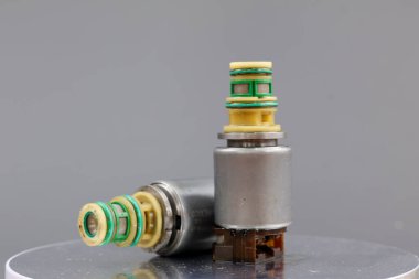 İki Allison iletim solenoid vanası gri bir arka planda gösteriliyor, biri dik duruyor ve diğeri yan tarafında. Fotoğraf metal gövdelerini, kablolarını ve konnektörlerini vurguluyor..