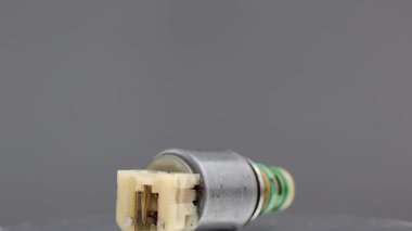 Katı gri arka planda sarı plastik konnektörü olan bir Allison Solenoid vanası. Fotoğraf, bu endüstriyel bölümün teknik detaylarını ve yıpranmış durumunu vurgulayan yakın plan bir fotoğraf..