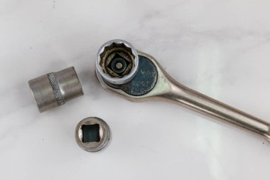 Bir grup endüstriyel alet, beyaz bir yüzeye yerleştirilmiş birkaç soket anahtarı ve birkaç soket içeriyor. Yakın plan çekimde metal dokuları ve amaçları ön plana çıkıyor..