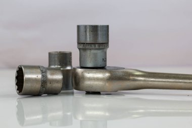 Bir grup endüstriyel alet, beyaz bir yüzeye yerleştirilmiş birkaç soket anahtarı ve birkaç soket içeriyor. Yakın plan çekimde metal dokuları ve amaçları ön plana çıkıyor..