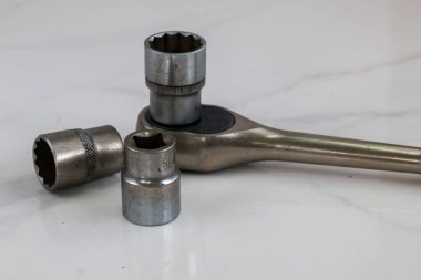 Bir grup endüstriyel alet, beyaz bir yüzeye yerleştirilmiş birkaç soket anahtarı ve birkaç soket içeriyor. Yakın plan çekimde metal dokuları ve amaçları ön plana çıkıyor..