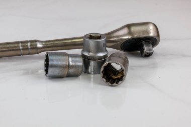 Bir grup endüstriyel alet, beyaz bir yüzeye yerleştirilmiş birkaç soket anahtarı ve birkaç soket içeriyor. Yakın plan çekimde metal dokuları ve amaçları ön plana çıkıyor..