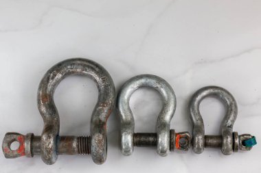 Üç farklı boyutta, ağır metal prangalardan oluşan bir grup, yatay olarak dizilmiş ve temiz beyaz bir yüzeye kurulmuş..