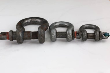 Üç farklı boyutta, ağır metal prangalardan oluşan bir grup, yatay olarak dizilmiş ve temiz beyaz bir yüzeye kurulmuş..