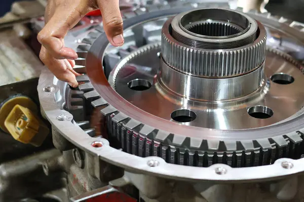 Bir tamircinin eli, detaylı bir motor tamiri veya bakım işlemi sırasında karmaşık bir iletim montajına debriyaj reaksiyon plakasını dikkatlice yerleştirir..