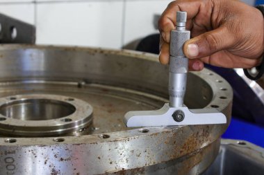 Endüstriyel metal bileşenini ölçmek için derinlik mikrometresi kullanan birinin yakın çekimi. Kalite kontrol ve hassasiyetin karmaşık süreci üzerinde duruluyor..