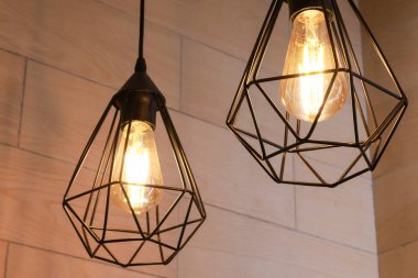 İki modern geometrik kolye lambası ve açıkta kalan Edison ampulleri ince desenli ahşap bir duvara karşı sıcak, davetkar bir parıltı saçıyor. Endüstriyel moda tasarımı her iç mekâna şık bir aksan katar..