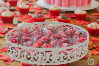 Sevgililer günü masası çilek şekeri ve keklerle dolu. Romantik bir ortam için kırmızı yapraklarla süslenmiş..