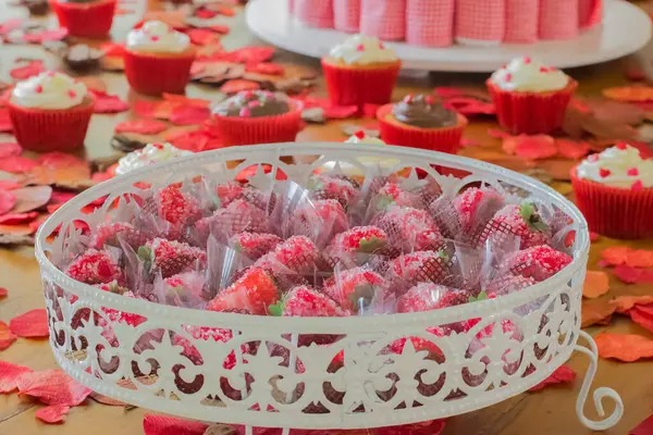 Sevgililer günü masası çilek şekeri ve keklerle dolu. Romantik bir ortam için kırmızı yapraklarla süslenmiş..