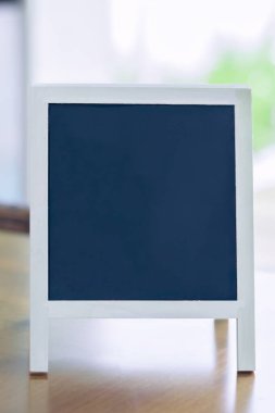 Tahta bir yüzeyde duran beyaz çerçeveli boş karatahta, kişiselleştirilebilir maketler, harfler, alıntılar, menüler veya promosyon mesajları için ideal.