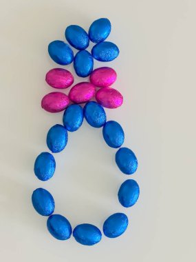 Mavi çikolatalı yumurtalar ve üstünde pembe bir fiyonk ile oluşan büyük Paskalya yumurtası, beyaz arka plan üzerinde renkli bir şenlik düzenliyor, tatil ve bahar kutlamaları için mükemmel..