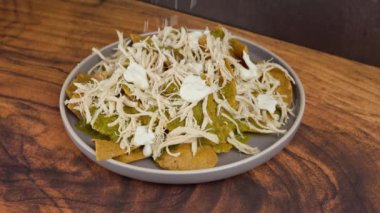 Chilaquiles yapmak için yeşil soslu mısır cipsinin üzerine rendelenmiş peynir serpiyorum.