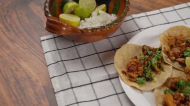Tahta bir masanın üzerinde beyaz kumaşlı tacos al pastor.