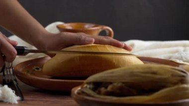 Latin bir kadın Meksika 'dan fırın gibi el yapımı bir Meksika kil tabağına tırtıklı bıçakla bolilo kesiyor.