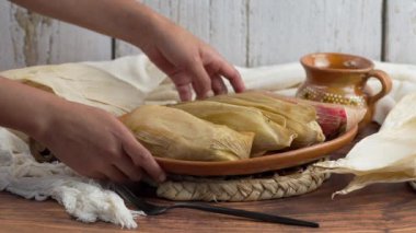 Latin kadın, Meksika mutfağında farklı tatlarda tamale içeren geleneksel bir kil tabağı gösteriyor.