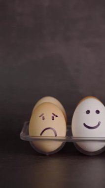 Dikey video, üzgün yüzlü kahverengi yumurta ve mutlu yüzlü beyaz yumurta, ruh halleri