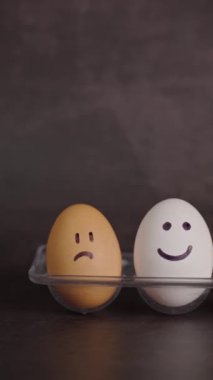 Dikey video, farklı ruh hallerinin gösterimi, üzgün yüzlü iki kahverengi yumurta ve mutlu yüzlü bir beyaz yumurta.