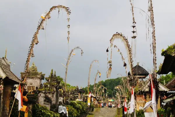 Penjor bambu kutupları Endonezya 'nın Bali kentindeki Penglipuran Köyü' nün taş sokağında dramatik bulutların altında. Geniş açılı. Seyahat, kültür, maneviyat ve sokak hayatı temalarına uyuyor. 21 Kasım 2024.