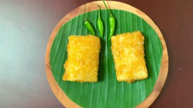 Muz yaprağı ahşap tabakta yeşil biberli iki altın gevrek pirzola yakın çekim 4K. Parlak, ayrıntılı ve canlı yemek, seyahat, tropikal yiyecekler ve görsel yaşam tarzı için ideal.