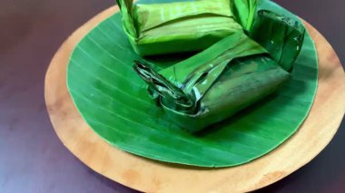 Tahta tabakta muz yaprağına sarılı cüzzamlının 4K görüntüsü. Yapışkan pirinç, taze tavuk dolgusu ve toprak aroması. Yemek, yaşam tarzı ve gelenek teması için mükemmel..