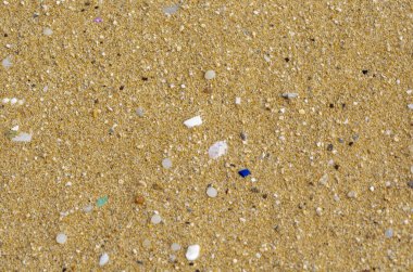 Altın kuma saçılmış mikro plastikleri kapatın. Plastik kirliliğinin plajlardaki çevresel sorunlarını vurguluyor. Farkındalık kampanyaları veya çevre dostu tartışmalar için uygundur