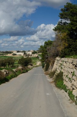 Taş duvarlar, canlı tarım alanları ve uzak tarihi binalarla çevrili pitoresk bir kırsal yol. Kırsal cazibenin ve zamansız mimarinin güzel bir tasviri.