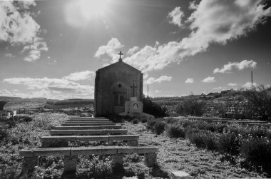 Huzurlu bir kırsal alanda, sıcak güneş ışığıyla yıkanmış büyüleyici bir taş şapel duruyor. Yeşillik ve basit taş banklarla çevrili kilise huzur ve manevi güzellik yayar.