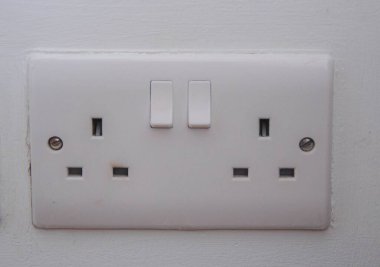 Beyaz bir Birleşik Krallık çift elektrik prizini kapatın. Her iki anahtar da kapalı, beyaz boyalı bir duvara monte edilmiş..