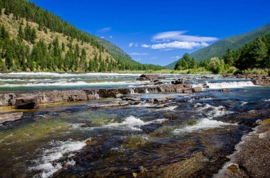 Berrak suların, yemyeşil ve görkemli dağlarla çevrili bir nehirdeki kayaların üzerinden hızla aktığı huzurlu bir manzara. Bu manzaralı nehir doğa, su ve manzara için ideal..