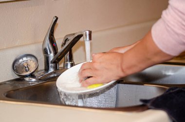 Mutfak lavabosunda akan suyun altında tabak yıkayan biri. Ev işleri, temizlik işleri ya da mutfak aktiviteleri için mükemmel.