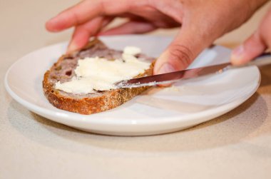 Bıçakla bir dilim ekmeğe tereyağı sürerken çekilmiş yakın plan bir fotoğraf. Yemek hazırlamak, kahvaltı etmek ve sağlıklı yemek için ideal.