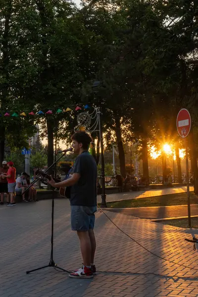 Bir sokak müzisyeni gitar çalar ve şarkı söyler. Gün batımının arka planına karşı duygusal bir ortam yaratır.