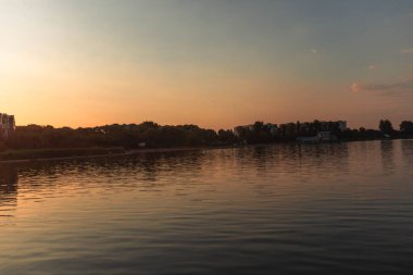 Arkasında günbatımı olan bir göl, ılık bir parıltı yayıyor.