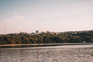 Sakin bir gölün yaz manzarası, uzak şehir hatlarıyla.
