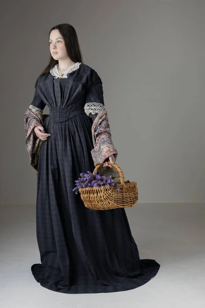 stock image A young Victorian woman wearing a blue cotton dress with vintage lace trim and holding a basket of lavender against a studio backdrop