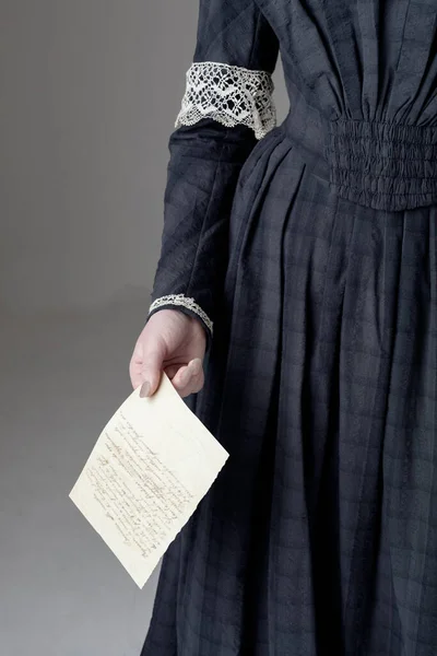若いビクトリア朝の女性がヴィンテージレーストリムと青の綿のドレスを着て スタジオの背景に手紙を持っています ロイヤリティフリーのストック写真