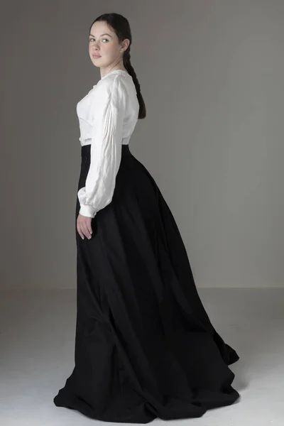 A young Victorian or Edwardian woman wearing a white linen Garibaldi blouse and black skirt