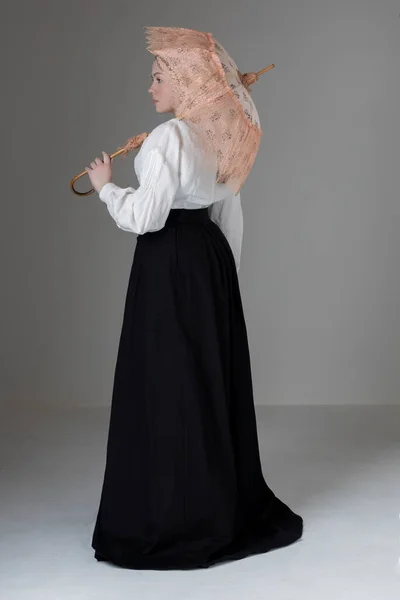 白のリネンを身に着けている若いビクトリア朝またはエドワード朝の女性ガリバルディブラウスと黒のスカートとヴィンテージパラソルを保持 ストックフォト