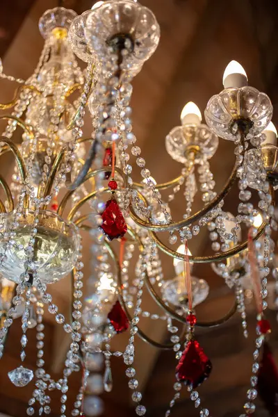 Vintage crystal chandelier with a red center crystal hanging below a wooden ceiling