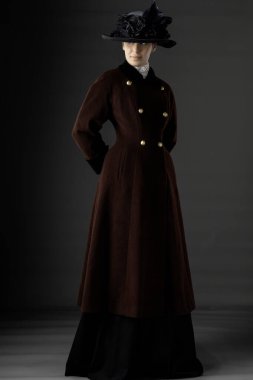 Victorian or Edwardian woman wearing a winter coat and hat against a studio backdrop clipart