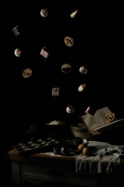 Pişmiş kurabiyeler, lamingtonlar, kremalar ve neenimsi turtalar eski bir yemek kitabından siyah bir arkaplana doğru havada süzülüyorlar.