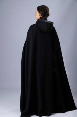 Kaba kahverengi keten kumaştan yapılmış etek giyen bir ortaçağ kadını. Uzun siyah saçları var, iki uzun örgü örüyor ve düz bir arkaplanda duruyor.
