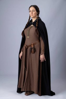 Kaba kahverengi keten kumaştan yapılmış etek giyen bir ortaçağ kadını. Uzun siyah saçları var, iki uzun örgü örüyor ve düz bir arkaplanda duruyor.